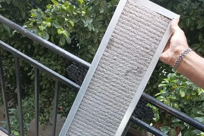 Tecnico che regge un filtro di climatizzatore ostruito dalla polvere, appena smontato